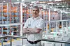 Volkswagen employee in white uniform stands with folded arms above a high-bay warehouse full of storage racks.