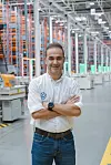 Volkswagen employee standing with folded arms in an automated warehouse aisle.