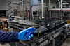 A gloved worker handling a battery module on an industrial assembly line in a factory.